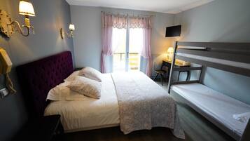 A bedroom with a large bed, a bunk bed, a desk, a chair, and a TV on the wall.