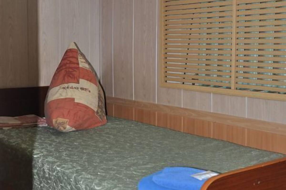 A single bed with a green mattress, a wooden headboard, a pillow, and a window with wooden blinds.