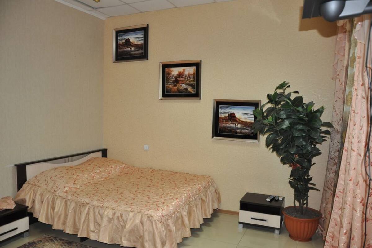 A bedroom with a bed, a nightstand, a potted plant, and three framed pictures on the wall.