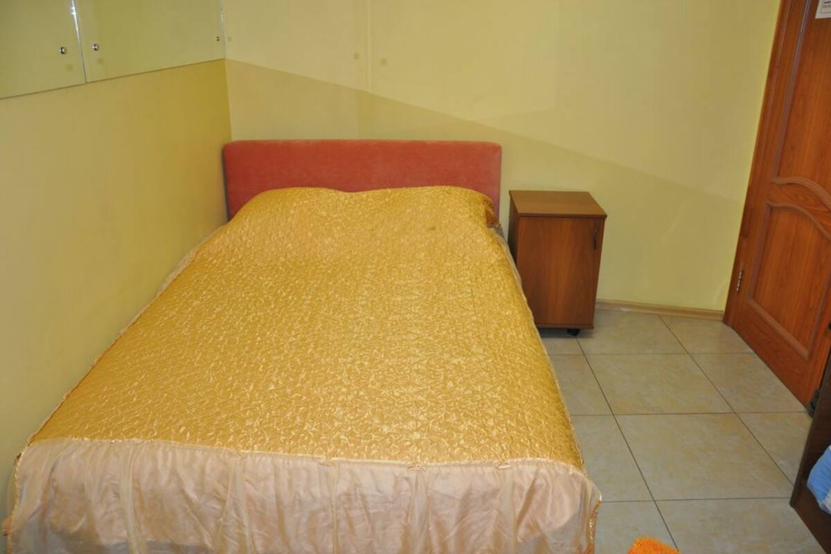 A single bed with a red headboard and a beige bedspread in a room with light yellow walls and a wooden door.