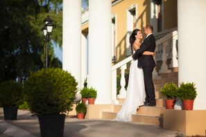 A couple embracing on a staircase with potted plants and a lamp post. - Hotel Plauter Kúria (Velky Meder)