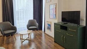 Una sala moderna con dos sillones, una mesa redonda pequeña, un aparador verde con cajones y un televisor de pantalla plana.