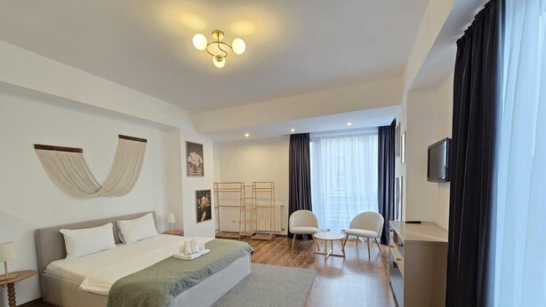 Una habitación de hotel moderna con una cama grande, un escritorio con dos sillas, un televisor y un ventanal con cortinas.