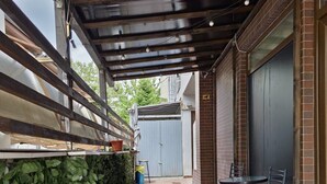 Un patio al aire libre cubierto con pared de ladrillo, cerca metálica y zona de estar con sillas y mesa.