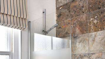 A modern bathroom with a glass-enclosed shower, a marble-tiled wall, and a white bathtub.