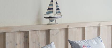 Un dormitorio con cabecera de madera, dos almohadas con motivos náuticos, una réplica de un pequeño velero y dos cuadros en la pared.