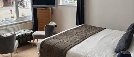 A hotel room with a bed, a TV, a desk, and a chair.
