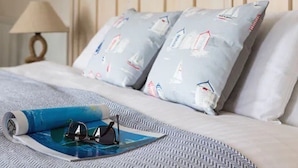 Ein ordentlich bezogenes Bett mit einem gemusterten Kopfkissen, einer aufgerollten Karte und einer Sonnenbrille.