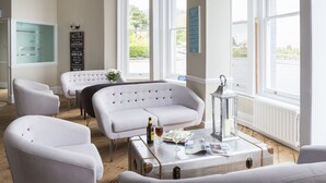 Ein Zimmer mit einem weißen Sofa, einem weißen Sessel, einem alten Koffer, einer Zeitschrift und einer Bierflasche auf einem Tisch.