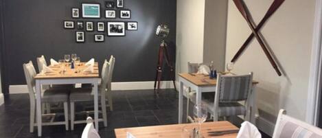 A dining area with two tables set for two, chairs, and a wall-mounted picture frame.