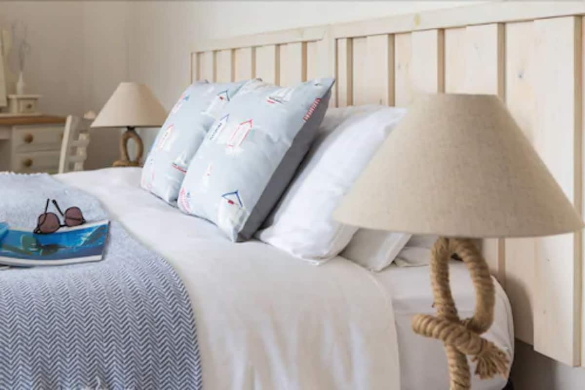 A neatly made bed with a striped blanket, a pair of sunglasses, and a book. There is a lamp with a rope base on the side.