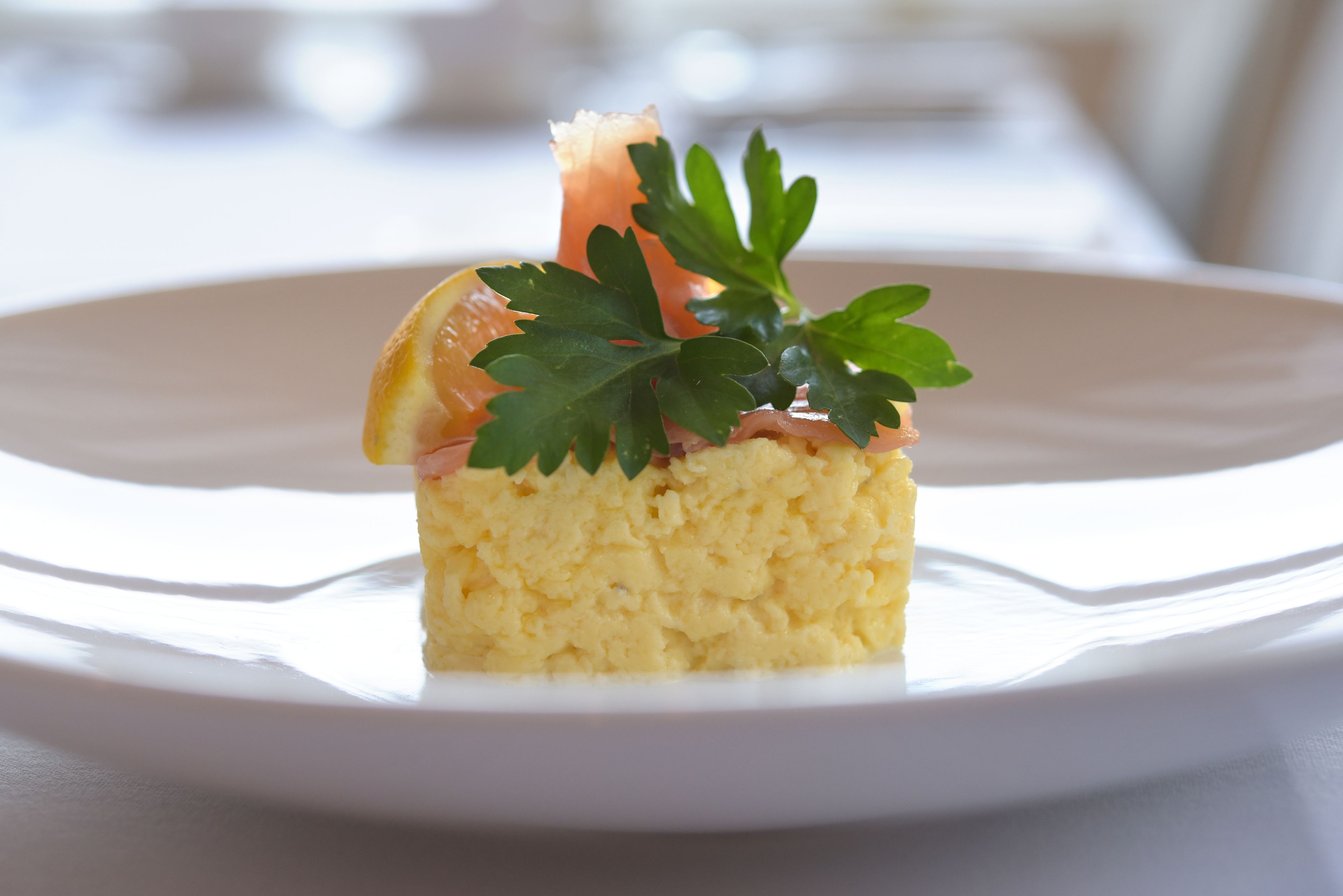 Une assiette blanche contenant un plat agrémenté de persil et d’une tranche d’orange.