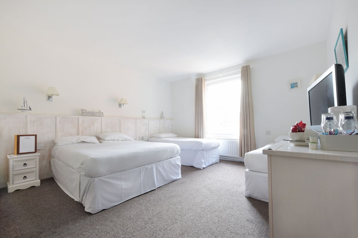 A hotel room with two beds, a desk, a chair, a TV, and a window with curtains.
