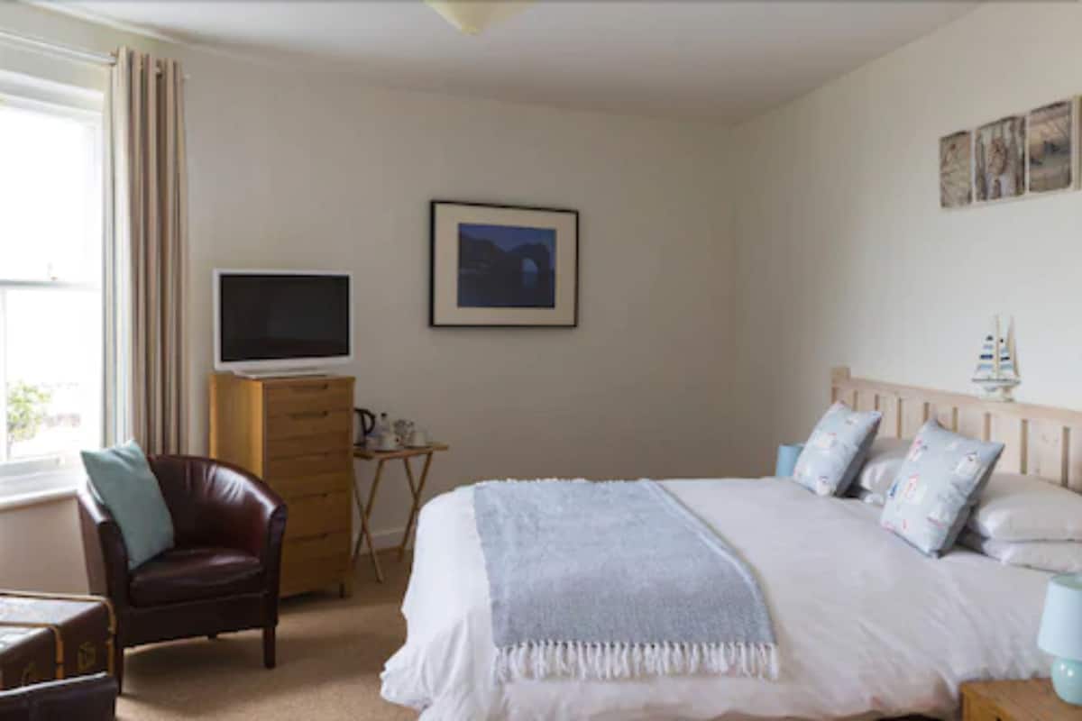 A bedroom with a bed, a chair, a dresser, a television, and artwork on the wall.