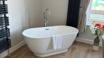 A bathroom with a freestanding bathtub, a radiator, a framed map on the wall, and a window with curtains.