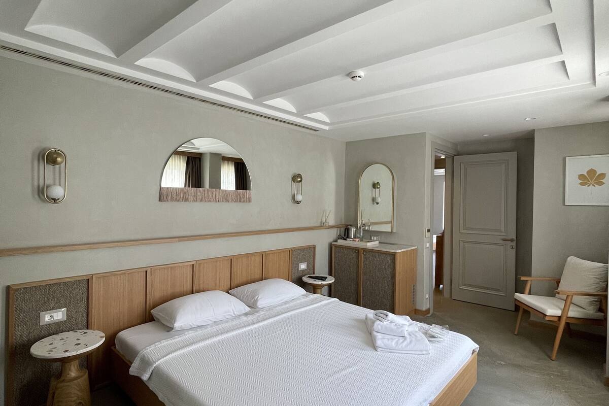 A modern hotel room with a large bed, a round mirror, a small table, and a chair.