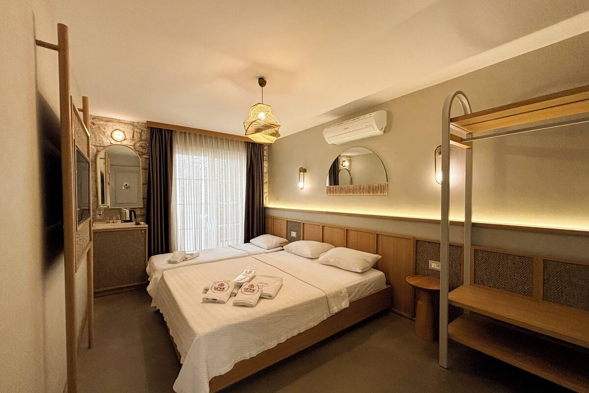 A hotel room with a bed, bedside tables, a mirror, a hanging light fixture, and a bunk bed.