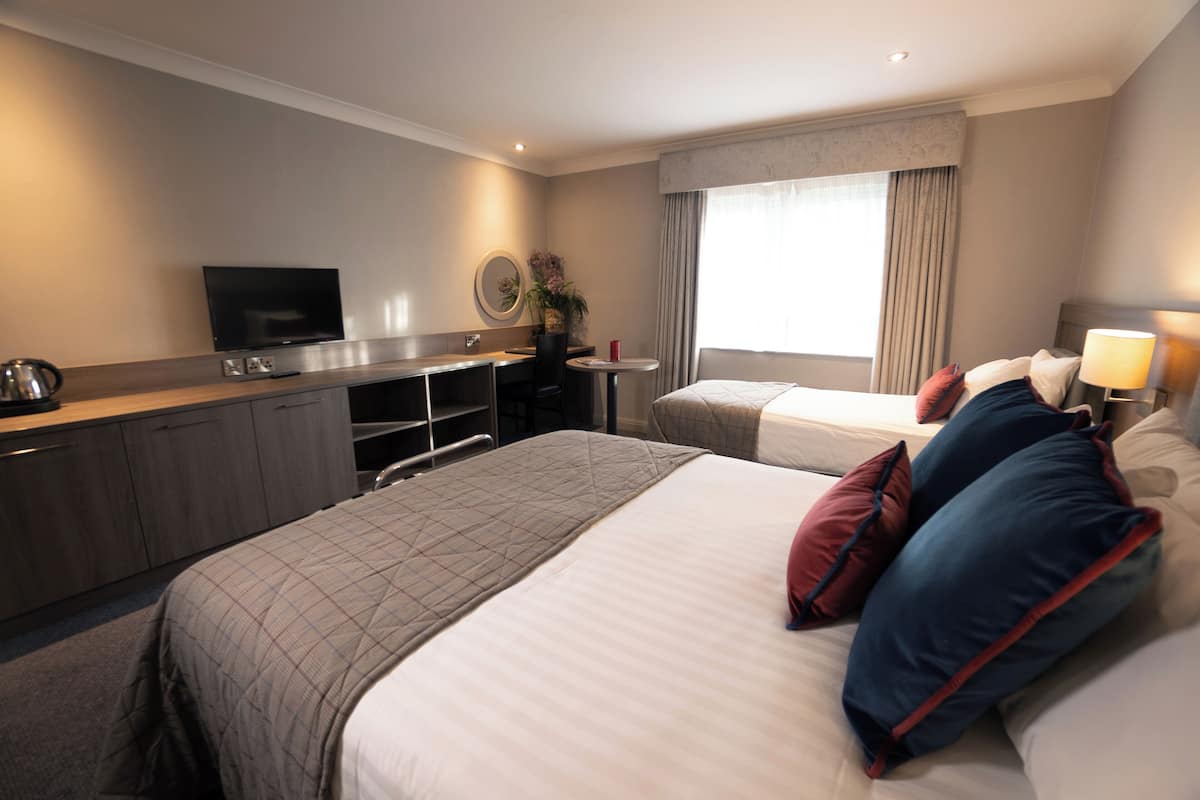A hotel room with two beds, a desk with a television, a small table, and a window with curtains.