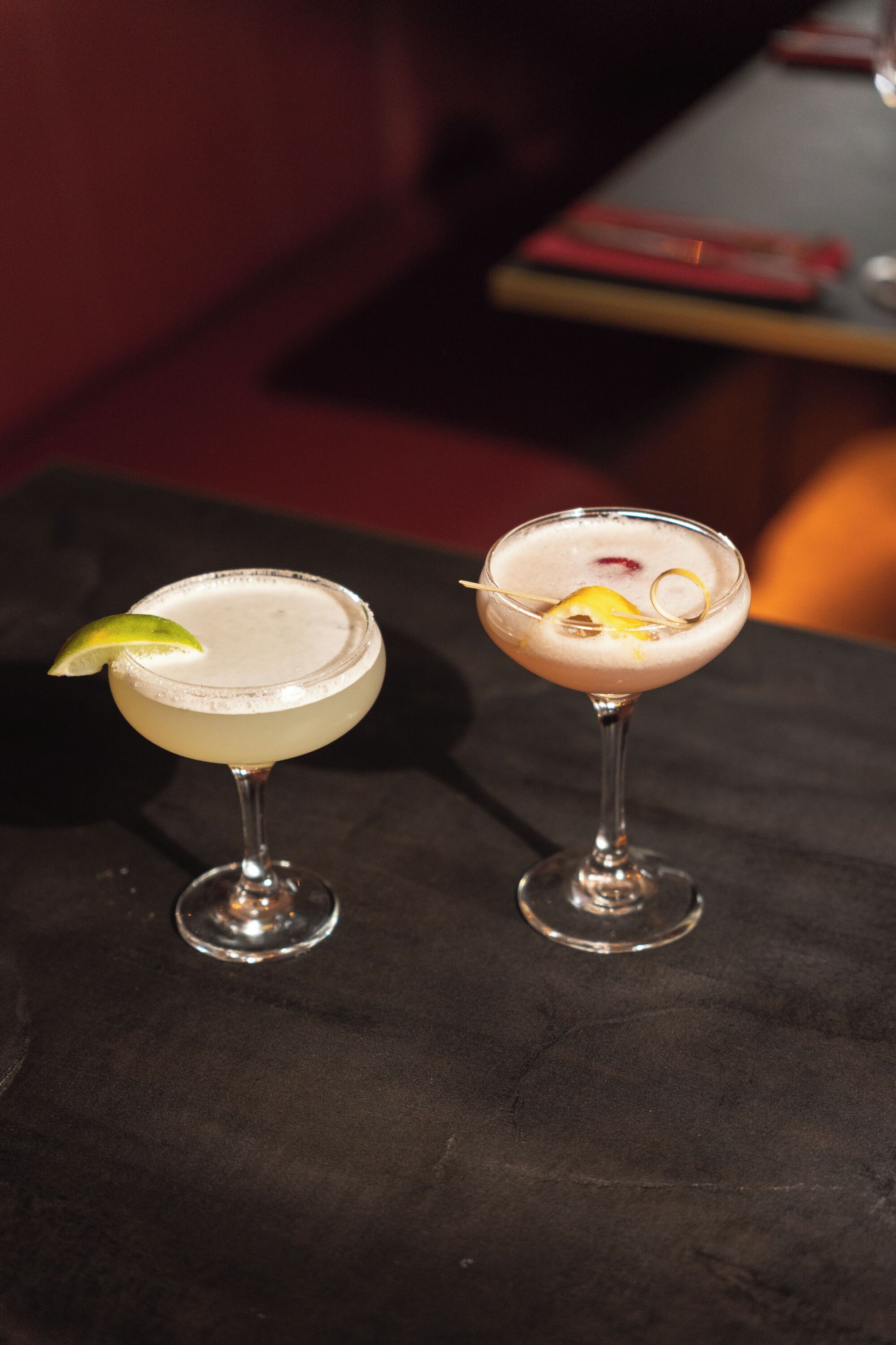 Two cocktails on a table with a dark surface.