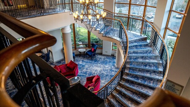 A spiral staircase with a view of a lobby area, including a chandelier and seating. - Seagoe Hotel (Craigavon)