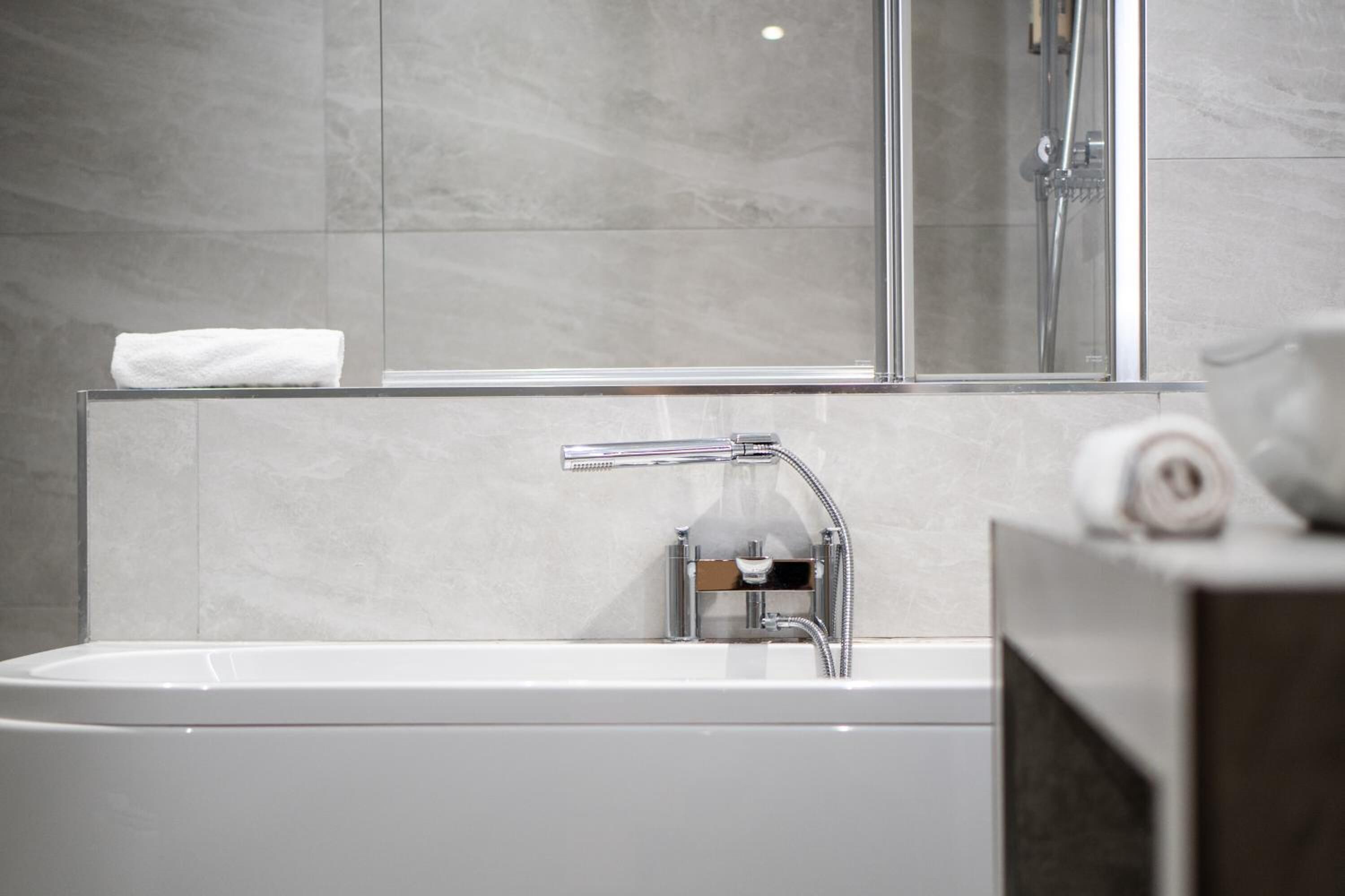 A modern bathroom with a white bathtub, a glass shower enclosure, and a towel on the edge of the tub.