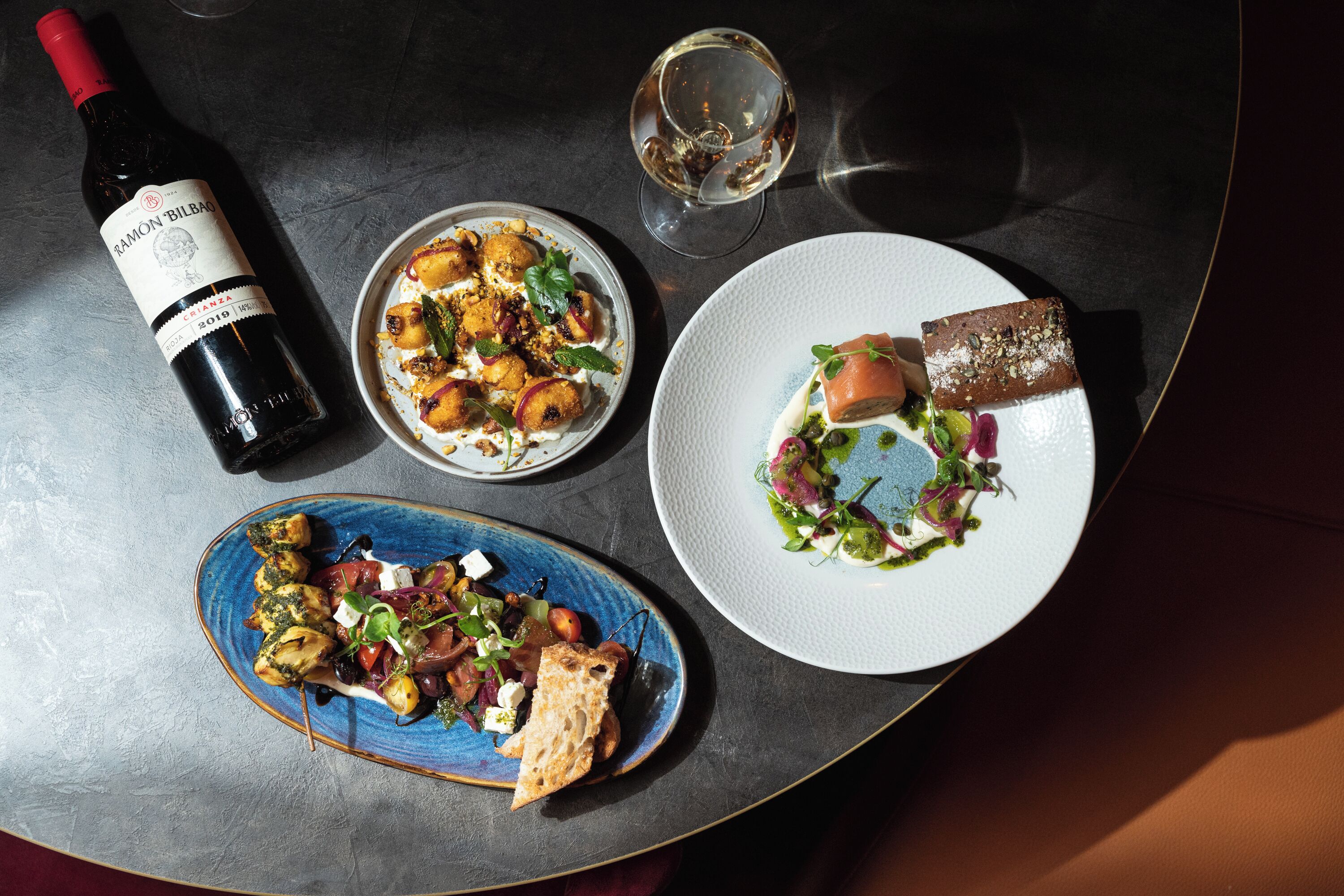 A table with a bottle of wine, two plates of food, and a glass of water.