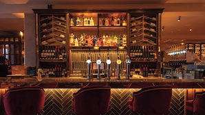 A bar area with multiple seating options, a variety of bottles and glasses on shelves, and a counter with a cash register. - Seagoe Hotel (Craigavon)