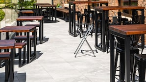 An outdoor patio with multiple wooden tables and chairs, a stone wall, and large windows. - Seagoe Hotel (Craigavon)