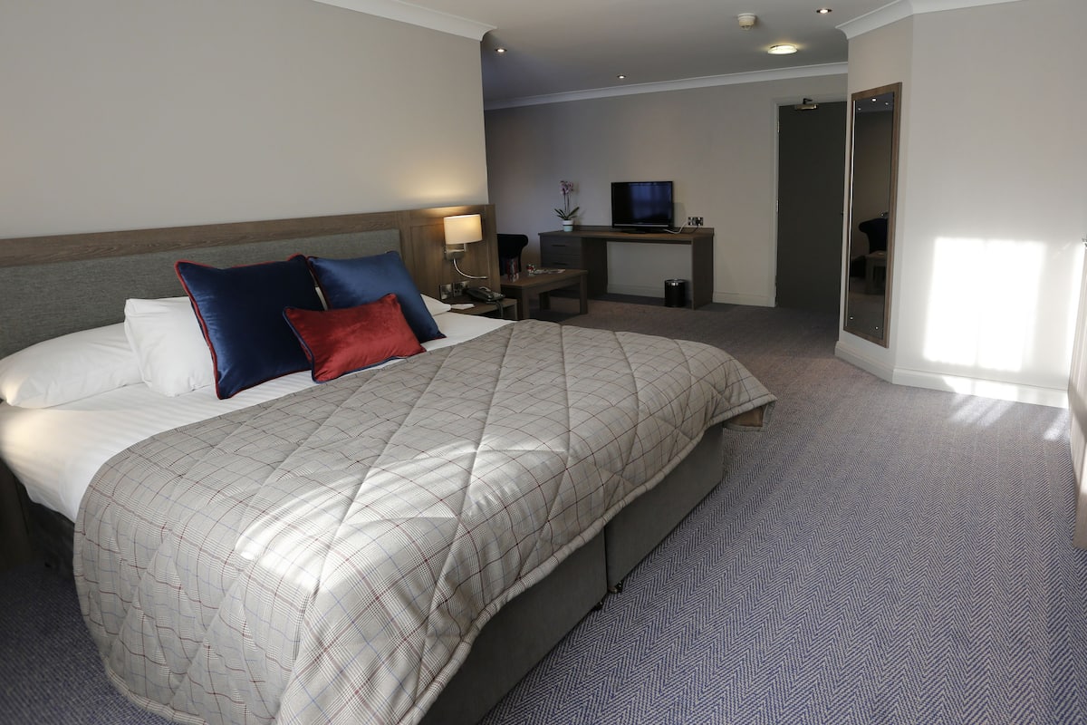 A hotel room with a large bed, a desk with a TV, and a mirror.