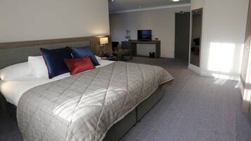 A hotel room with a large bed, a desk with a TV, and a mirror.