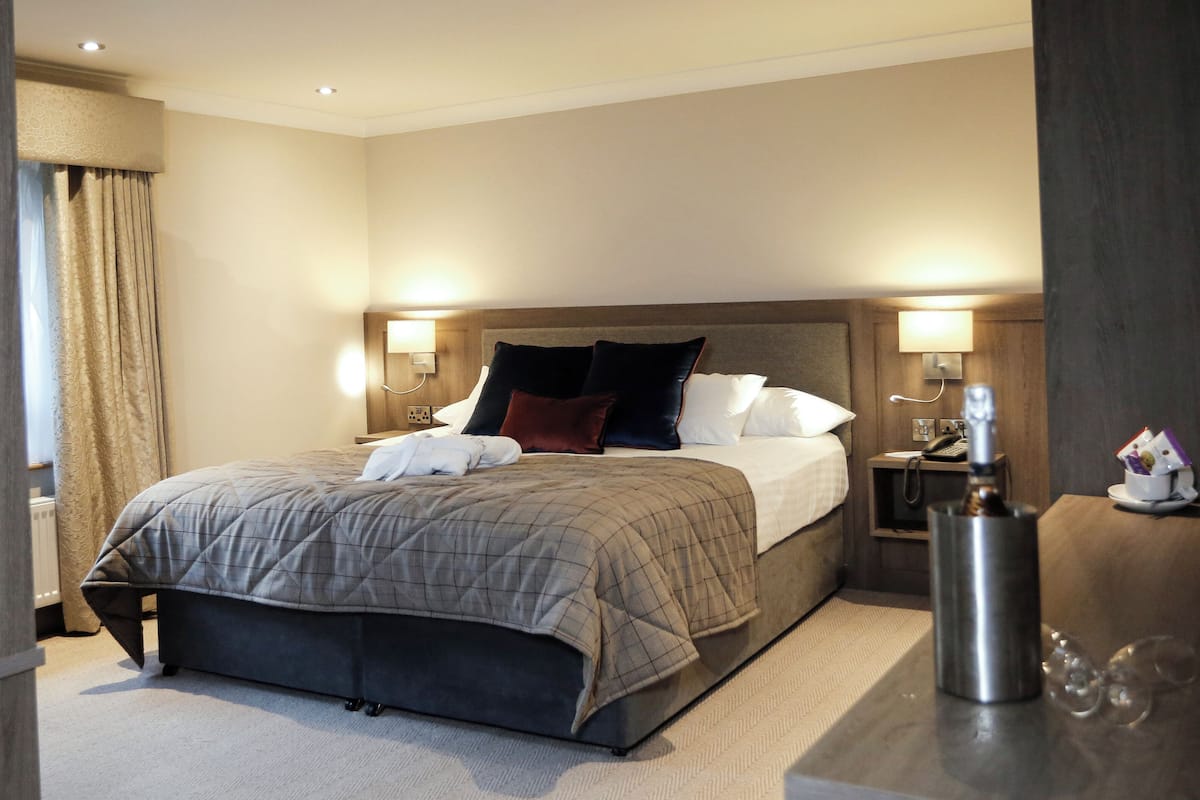 A hotel room with a large bed, two bedside tables, a nightstand, a lamp, and a bottle on the nightstand.
