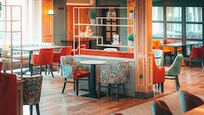 A modern interior with a central dining table surrounded by colorful chairs, wooden shelves with decorative items, and large windows allowing natural light. - Seagoe Hotel (Craigavon)