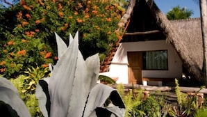 A thatched-roof house surrounded by lush greenery and flowering plants. - Palmeiras Lodge (Vilanculos)