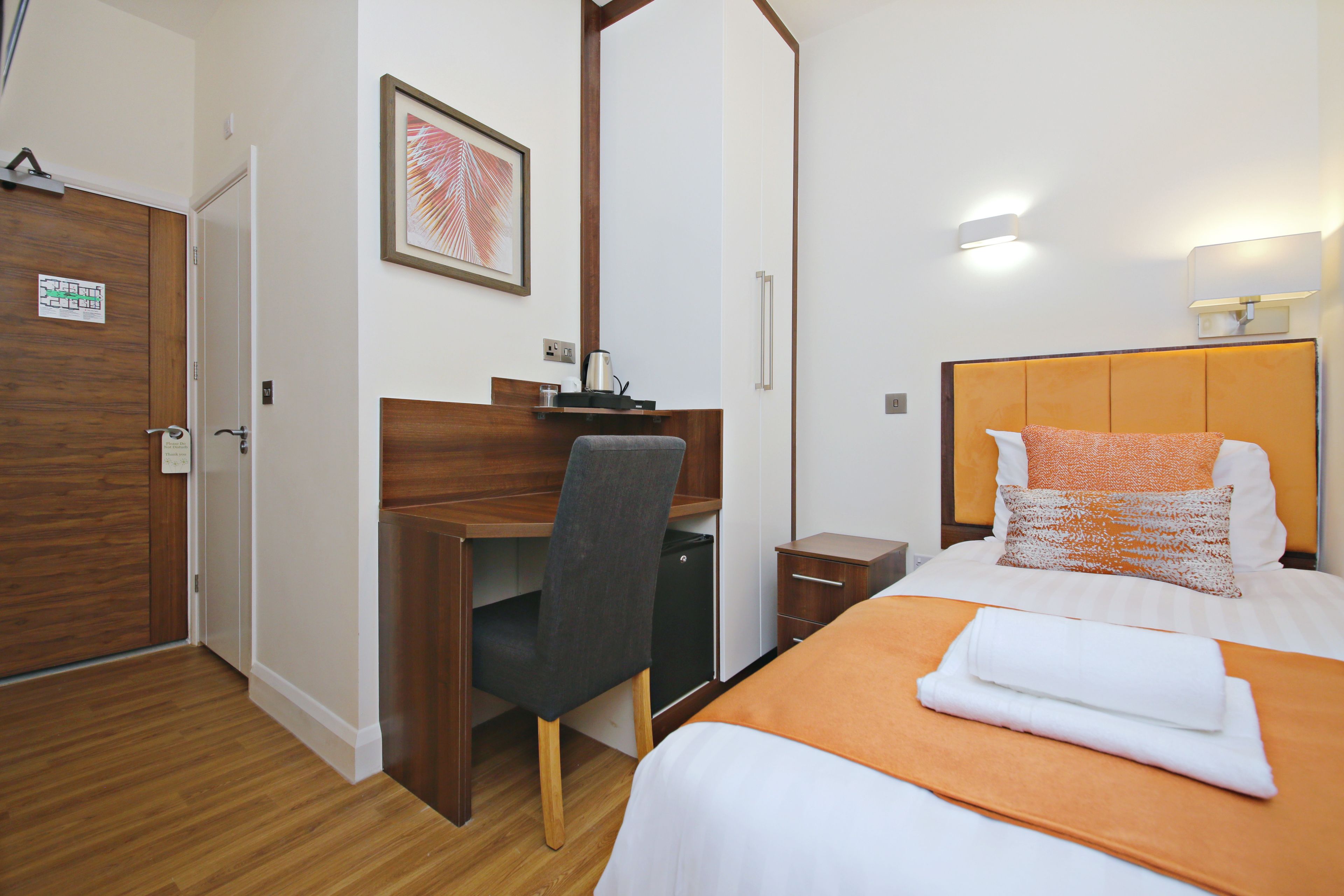 Ein Hotelzimmer mit Schreibtisch aus Holz, einem Bett mit orangefarbener Bettdecke und einem gerahmten Bild an der Wand.