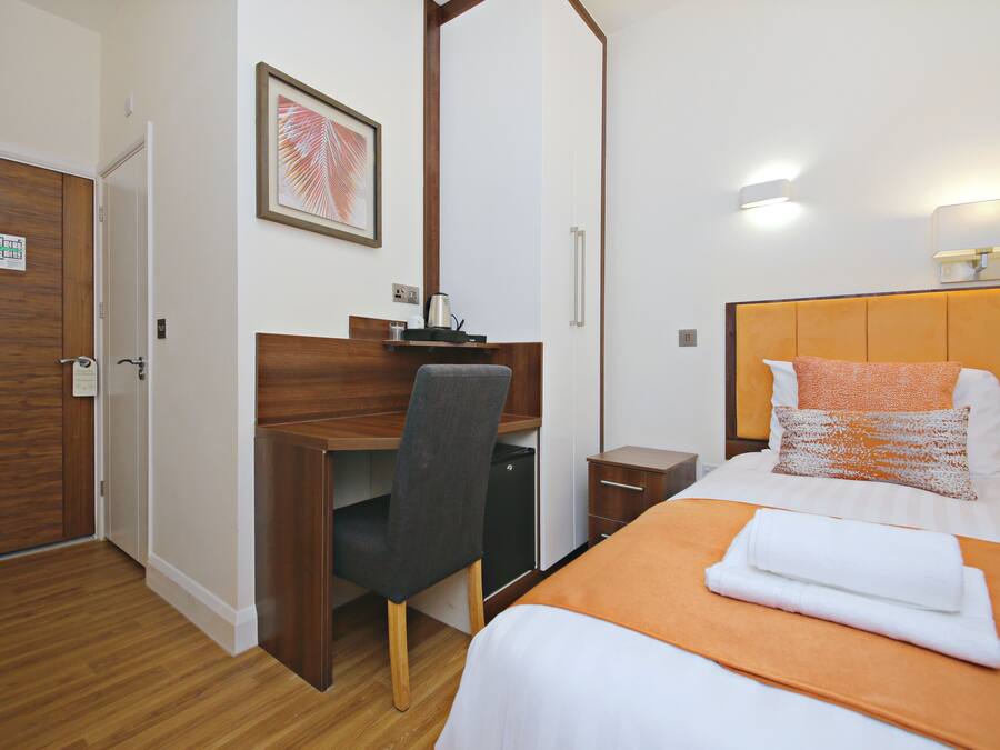 Ein Hotelzimmer mit Schreibtisch aus Holz, einem Bett mit orangefarbener Bettdecke und einem gerahmten Bild an der Wand.