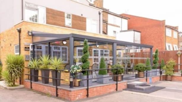 A modern building with a glass-enclosed patio area, surrounded by brick walls and potted plants. - Imperial Guest House (Hounslow)