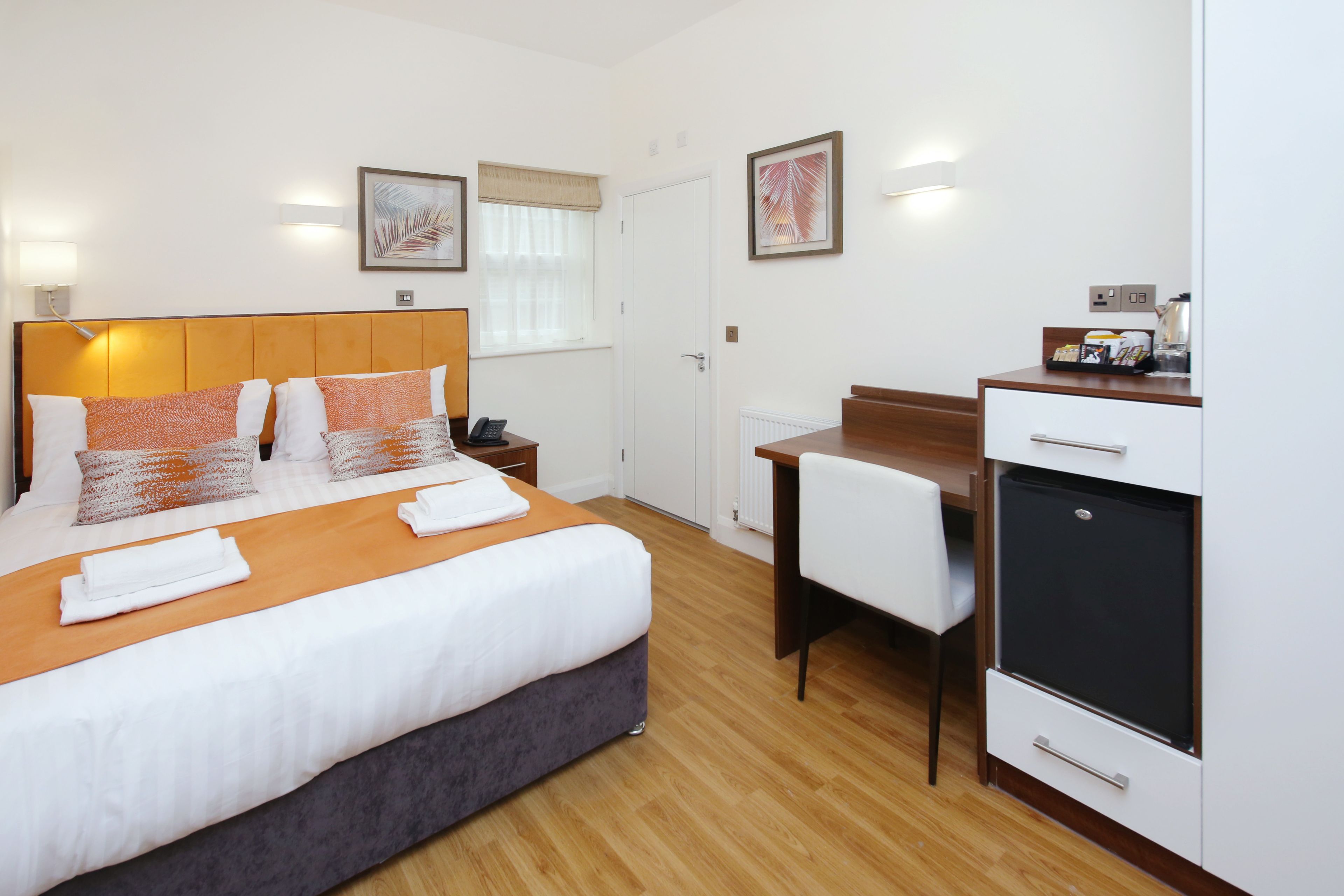 Habitación de hotel con cama, escritorio, silla, refrigerador y ventana con cortinas.