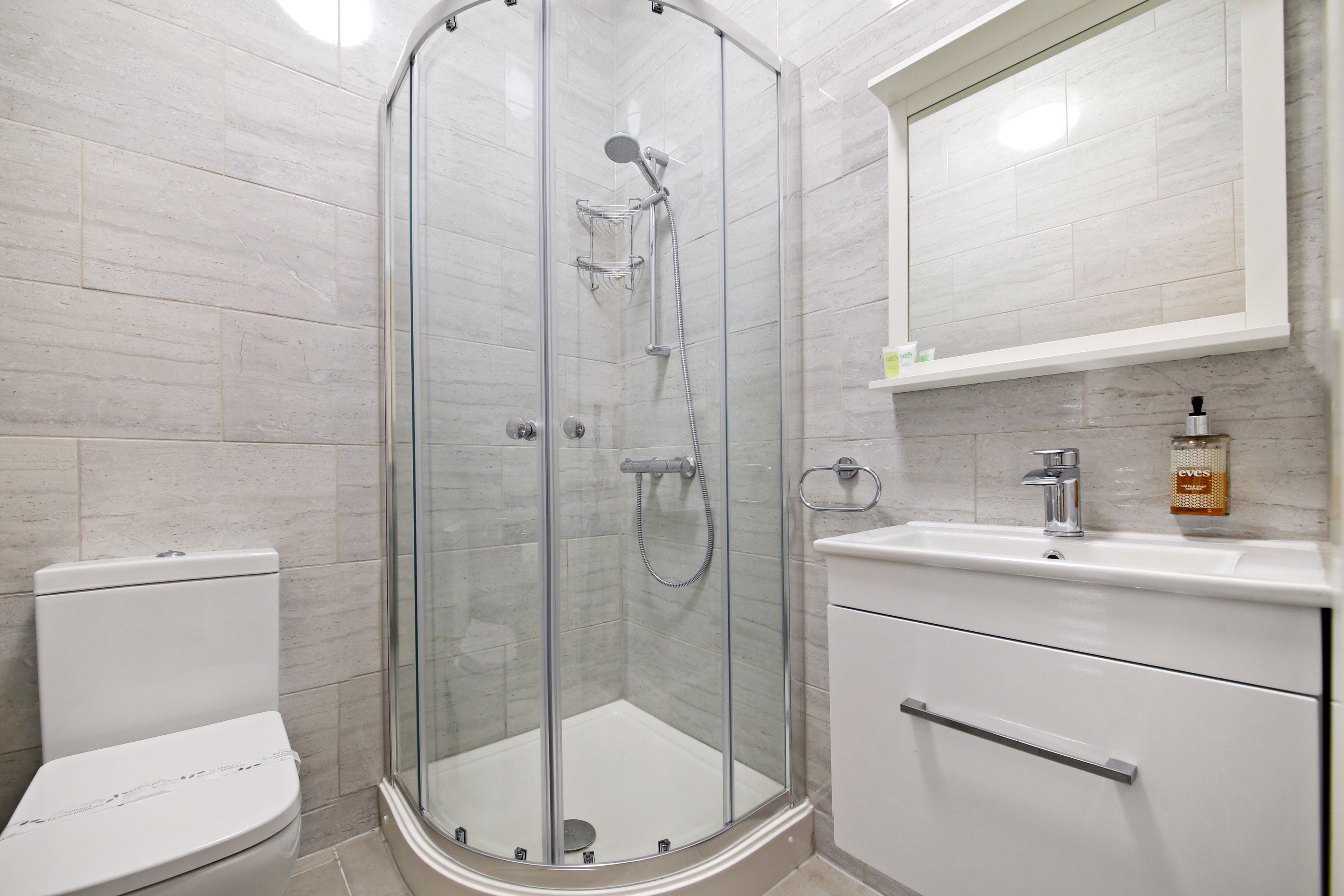 A modern bathroom with a glass-enclosed shower, a white toilet, and a sink with a soap dispenser.