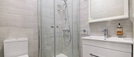 A modern bathroom with a glass-enclosed shower, a white toilet, and a sink with a soap dispenser.