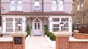 A two-story building with a symmetrical facade, numbered 28, featuring a central entrance with a white door, flanked by two lamp posts and small potted plants. - Imperial Guest House (Hounslow)