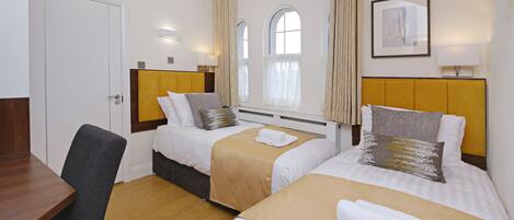 A hotel room with two beds, a wooden desk, and a window with curtains.