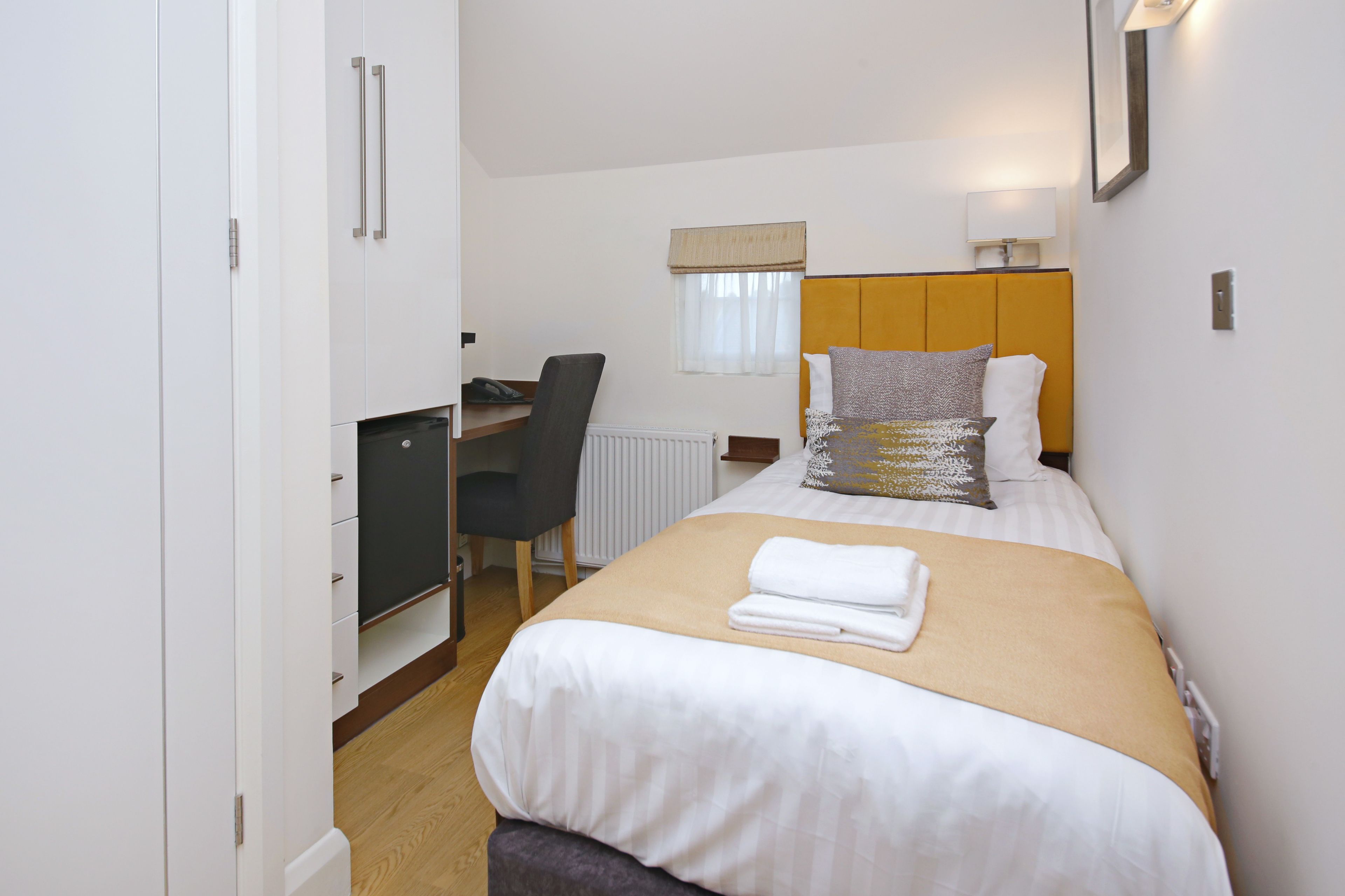 A hotel room with a bed, a desk, a chair, and a radiator.