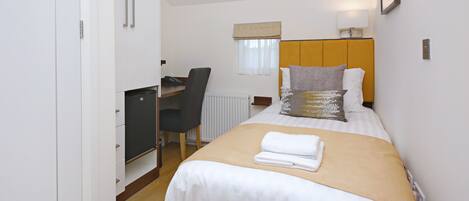 A hotel room with a bed, a desk, a chair, and a radiator.