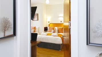 Una habitación de hotel moderna con suelo de madera, una cama con ropa de cama blanca y naranja, un banco gris y un cuadro en la pared.