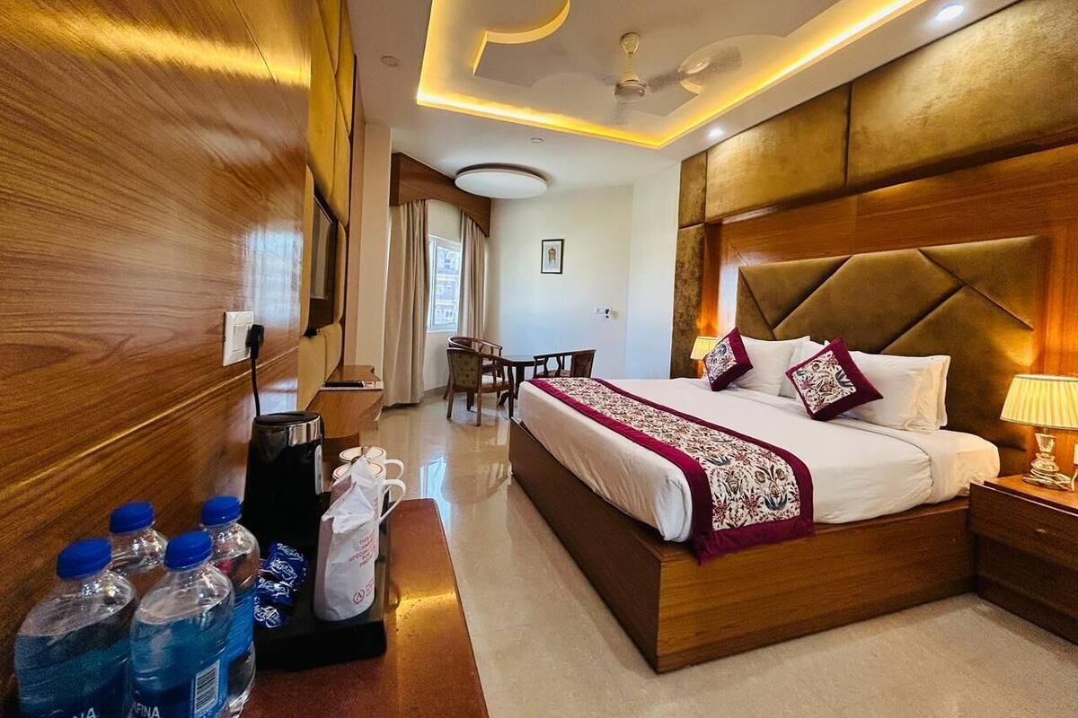 Ein Hotelzimmer mit einem großen Bett, einem Holz-Kopfteil, einem Schreibtisch mit Stuhl und einem Essbereich mit Tisch und Stühlen.