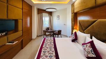 A hotel room with a bed, a television, a dining table with chairs, and a ceiling fan.