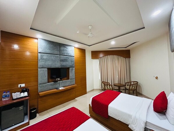 A hotel room with two beds, a TV, a small table, and a seating area.