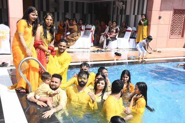 Un grupo de personas en una zona de piscina, algunas con ropa amarilla, con un escenario y sillas al fondo.