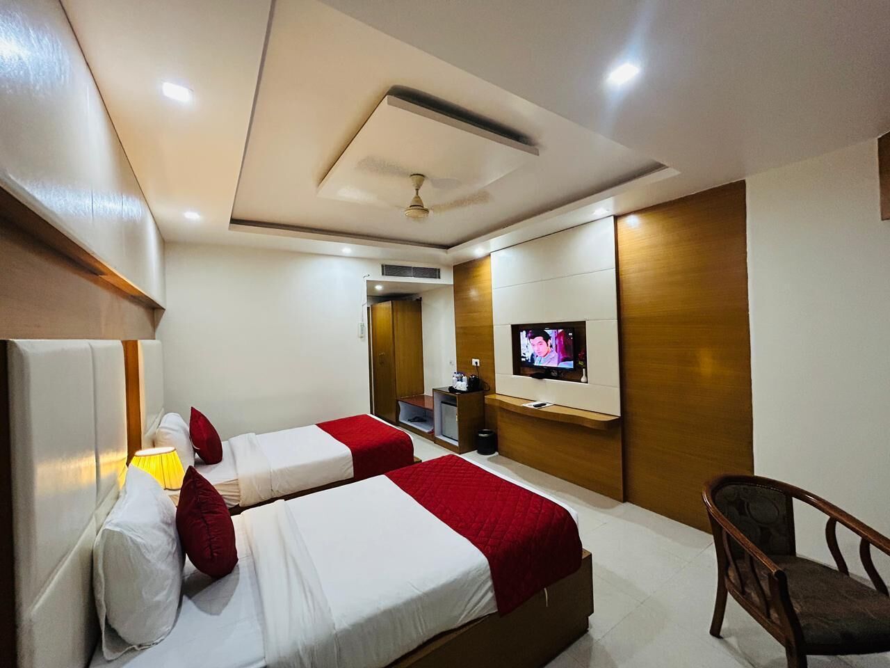 A hotel room with two beds, a TV, a chair, and a wooden panel wall.