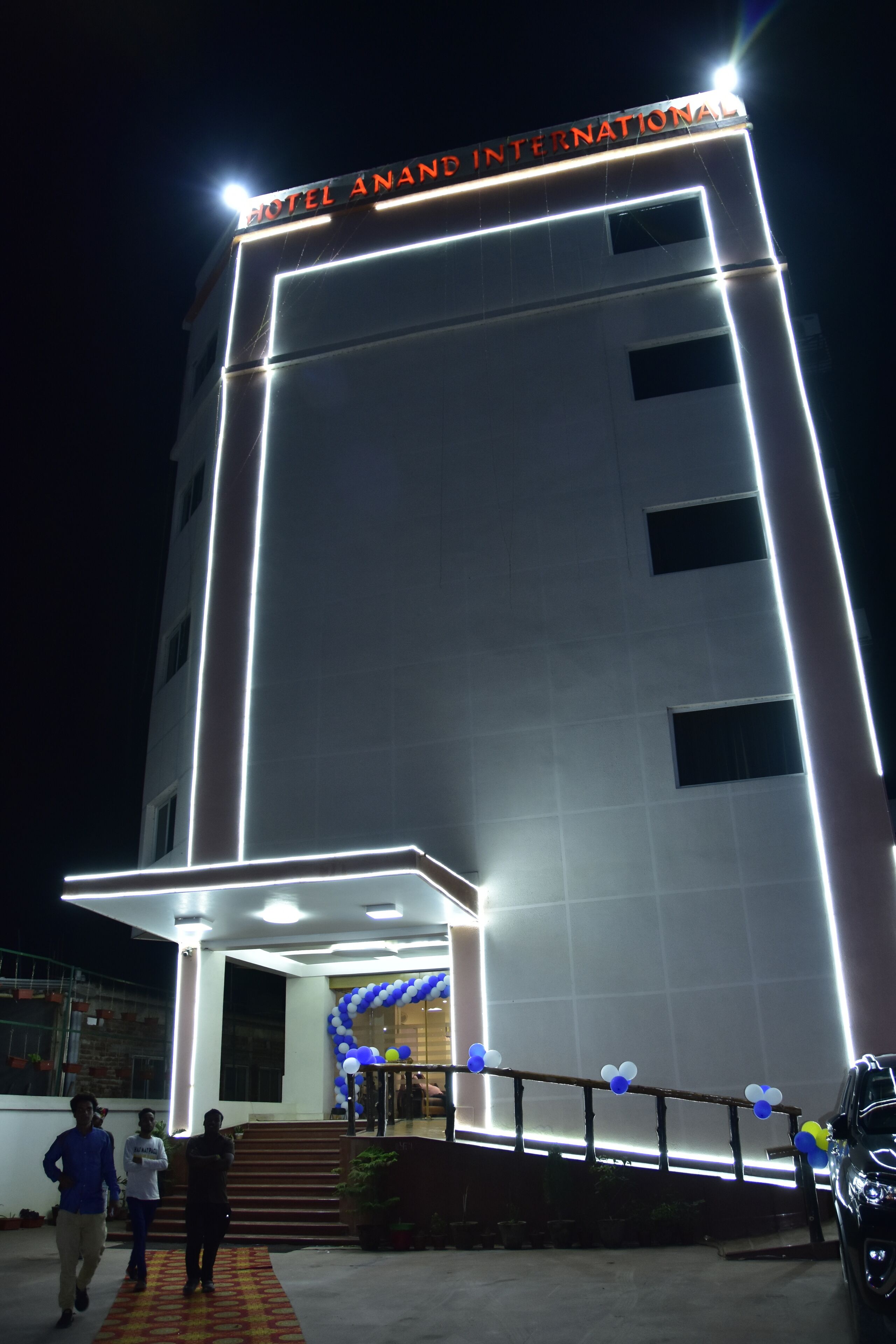 Un hotel con una facciata moderna, insegne illuminate e un ingresso accogliente con gradini e un arco decorativo.
